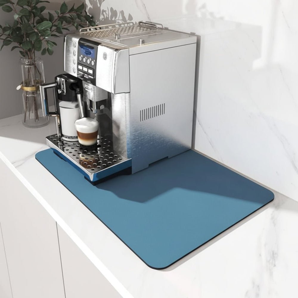 Blå rektangulär matta på en marmorbänk under en silverfärgad kaffemaskin med en latte i koppen, sedd snett uppifrån. 1