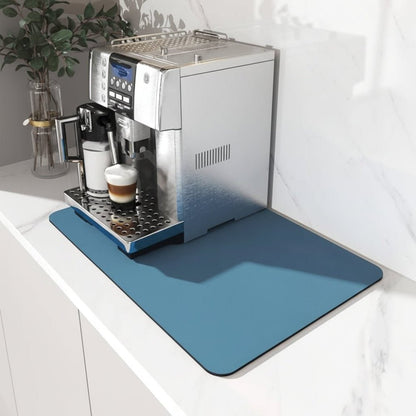 Blå rektangulär matta på en marmorbänk under en silverfärgad kaffemaskin med en latte i koppen, sedd snett uppifrån. 1