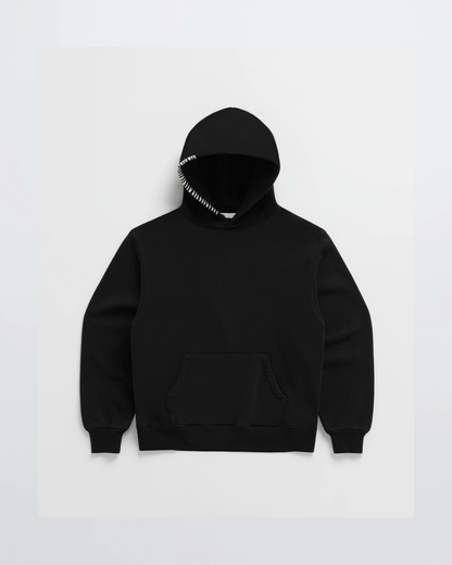 Svart hoodie sedd framifrån, med känguruficka och kontrasterande vit dekorsöm längs ena huvkanten. 5