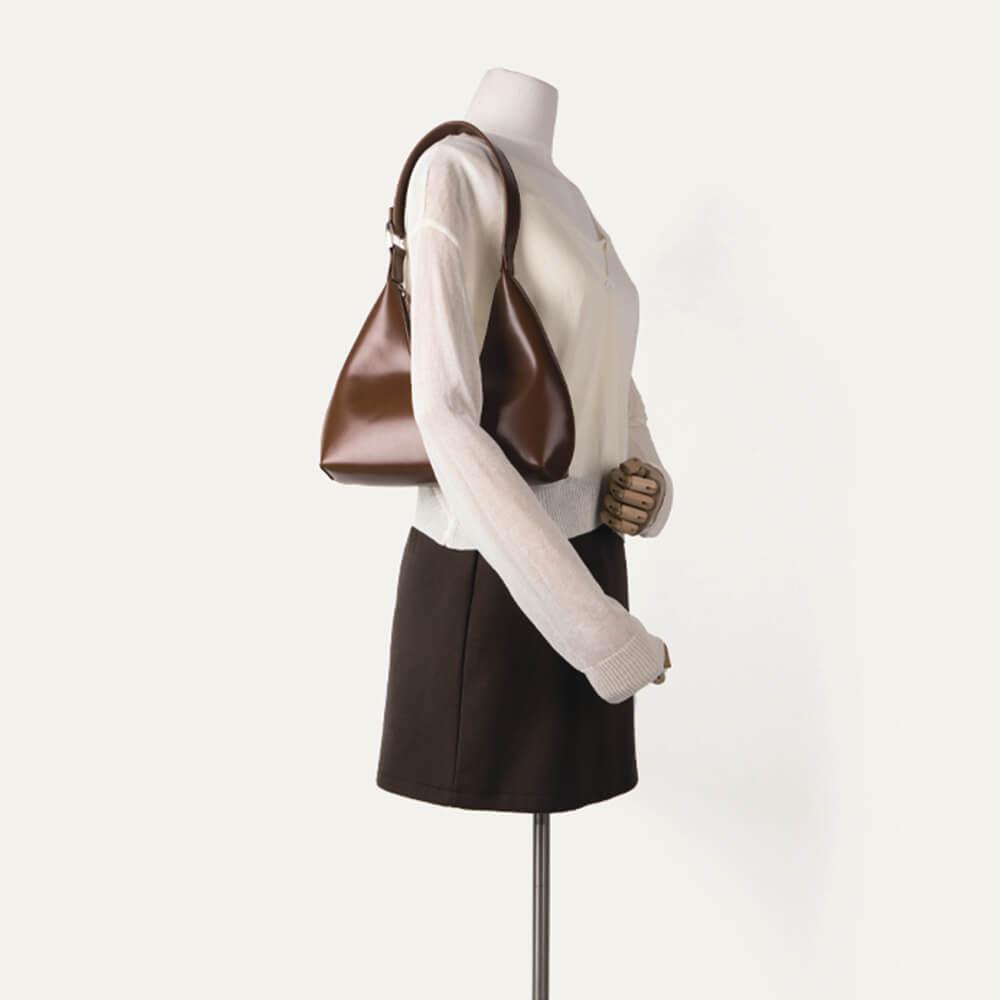 Braune, tragbare Halbmondtasche aus Leder auf Schaufensterpuppe, modisch und elegant.