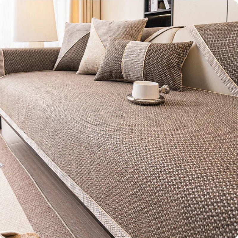 Soffa med brunt överdrag i vävd struktur, kuddar i brunt och beige samt en vit kopp på sittytan. 10
