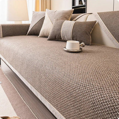 Soffa med brunt överdrag i vävd struktur, kuddar i brunt och beige samt en vit kopp på sittytan. 10