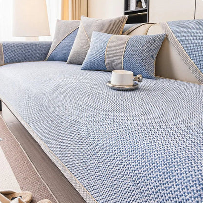 Soffa med ljusblått överdrag i vävd struktur, blå och grå kuddar samt en vit kopp på sittytan. 11