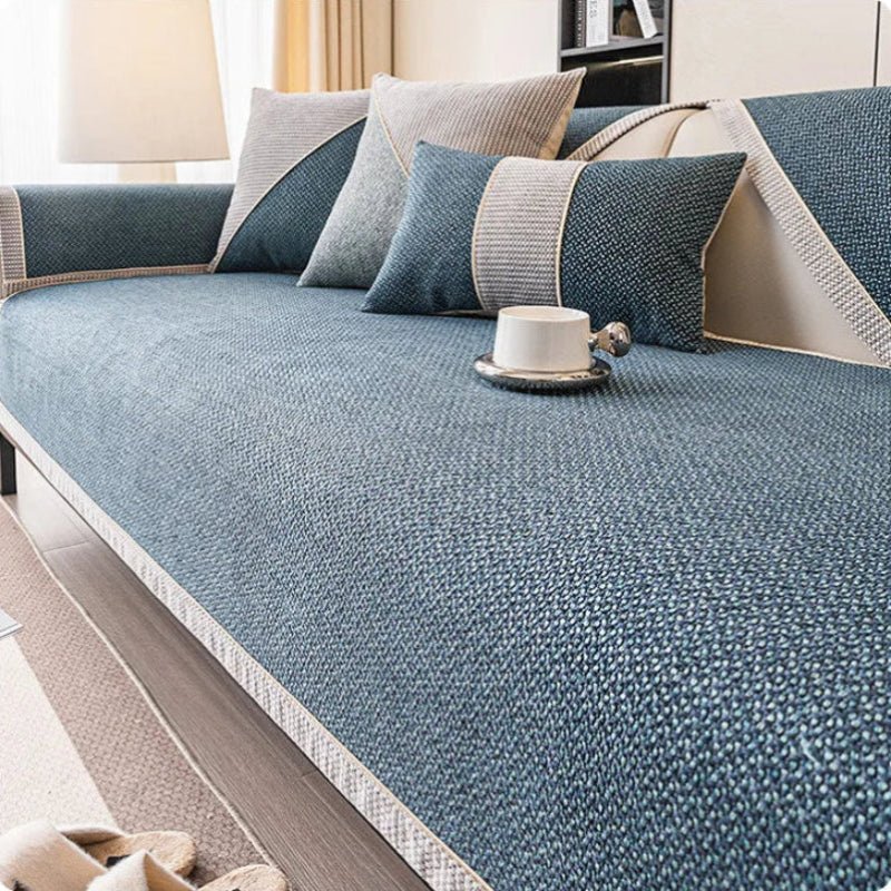 Soffa med blågrönt överdrag i vävd struktur, grå och blå kuddar samt en vit kopp på sittytan. 8