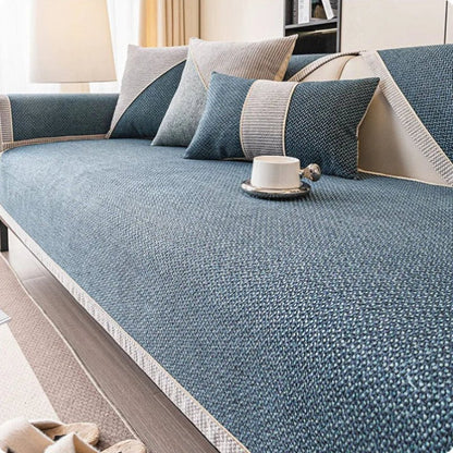 Soffa med blågrönt överdrag i vävd struktur, grå och blå kuddar samt en vit kopp på sittytan. 8