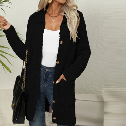 Frau in schwarzem Strickmantel, weiße Bluse, Jeans, goldene Kette, Handtasche, modisch.