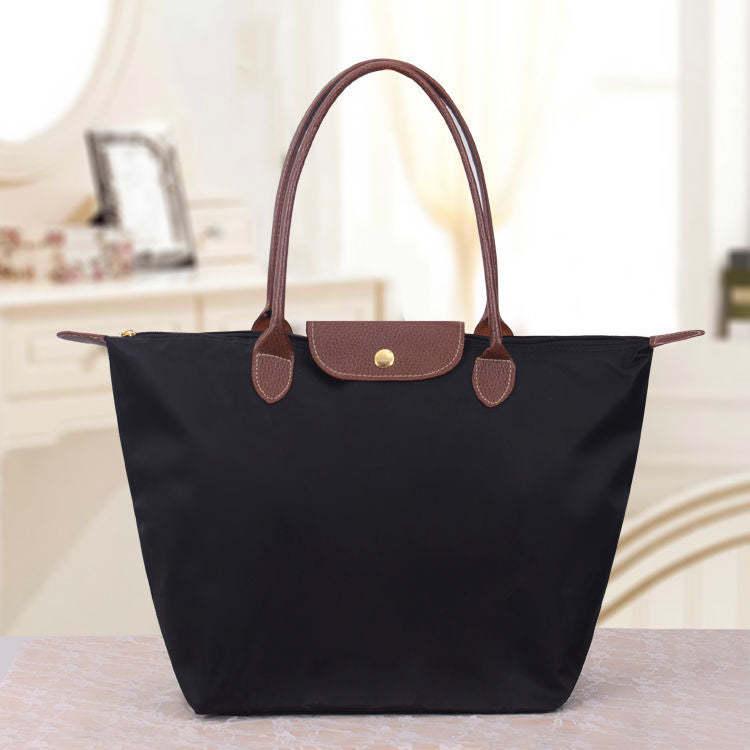Schwarze Handtasche aus Leder und Nylon mit braunen Griffen auf einem Tisch im eleganten Raum.