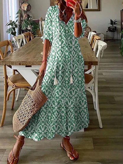 Frau in grünem Sommerkleid mit Muster, Strohtasche, Sandalen, Esszimmer im Hintergrund.