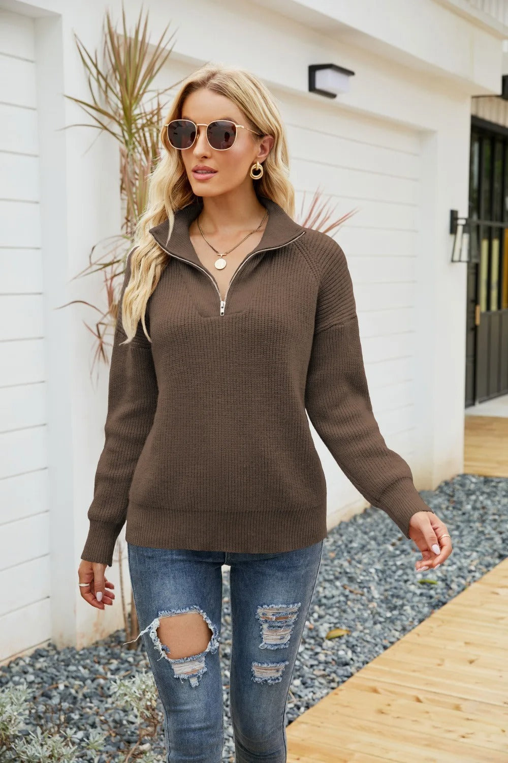 Frau in braunem Strickpullover, Reißverschluss, Sonnenbrille, zerrissene Jeans, draußen.