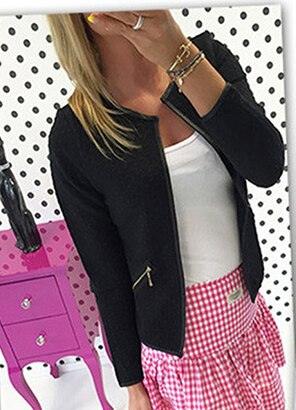 Frau in schwarzer Jacke mit Reißverschluss, weißem Top und rosa kariertem Rock vor gepunkteter Wand.