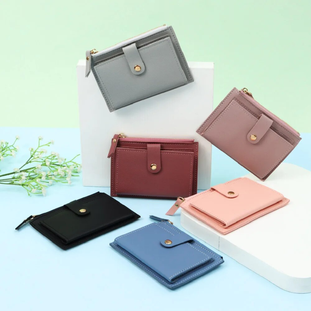 Fünf Mini-Geldbörsen aus Leder in Grau, Rosa, Schwarz, Blau und Rot auf pastellfarbenem Hintergrund.