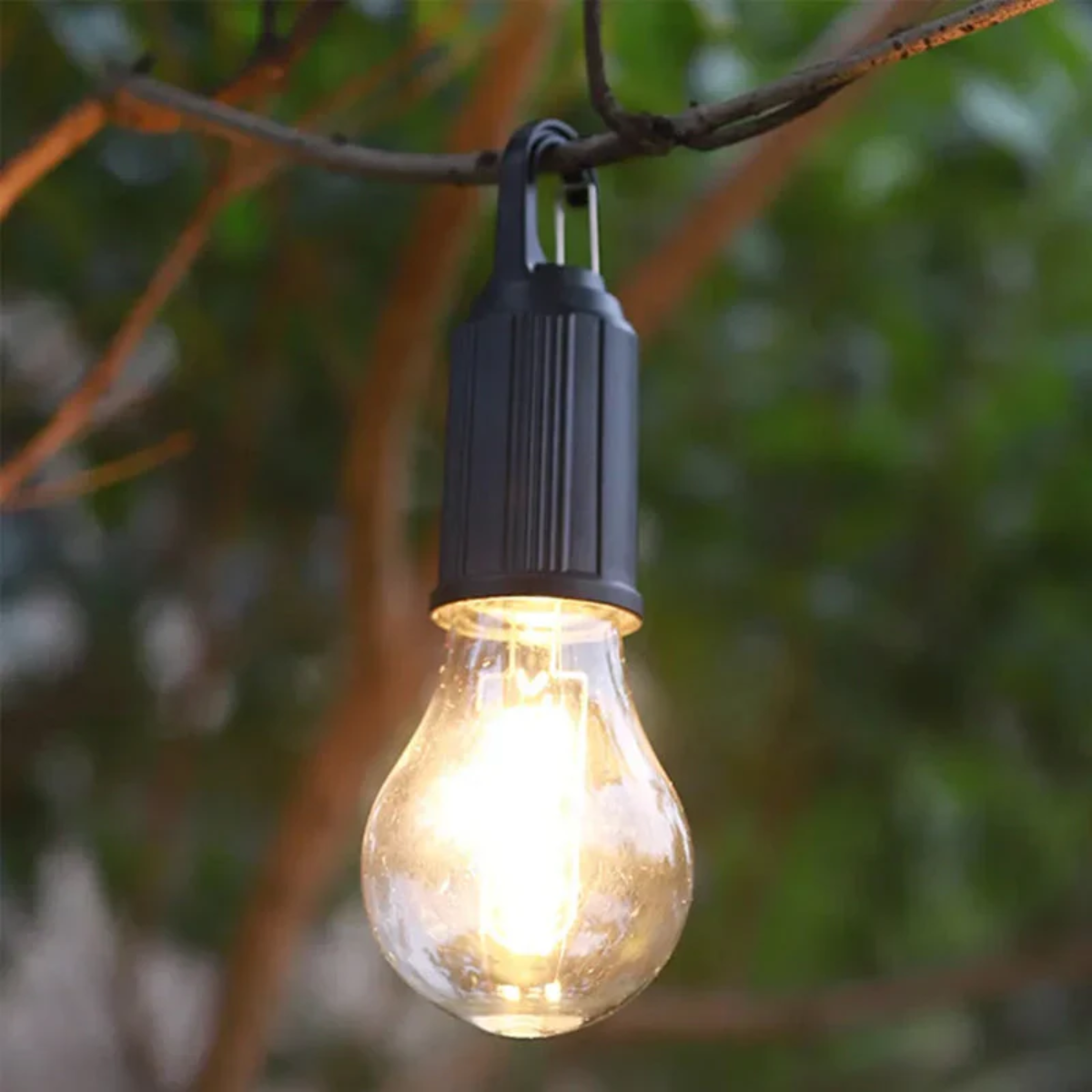 Tänd lampa med varm glöd hängd på en gren mot suddig grön bakgrund 10