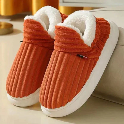 Ett par ribbade plyschtofflor i orangerött med vitt fluffigt foder och tjock vit sula, lutade mot en soffa. 6