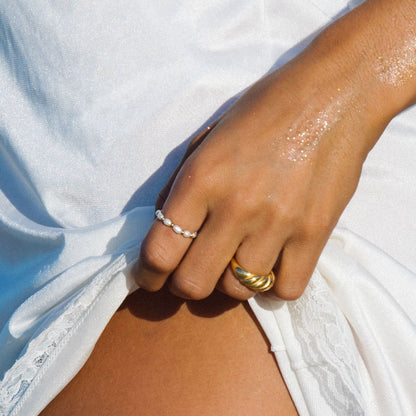 Hand mit wasserdichten Ringen, Gold und Perlen, auf weißem Stoff.