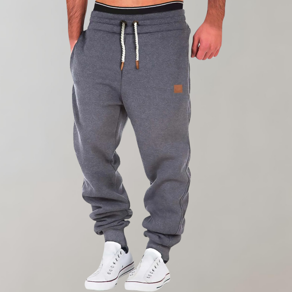 Mörkgrå joggerbyxor med vit dragsko och elastisk midja, burna med vita sneakers 2