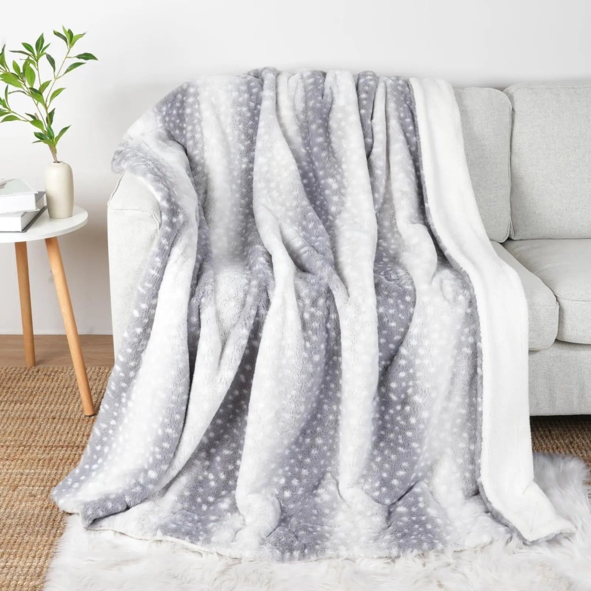 Pläd i grått och vitt med samma fläckmönster draperad över en ljus soffa, med vit sherpa på kanten. 7