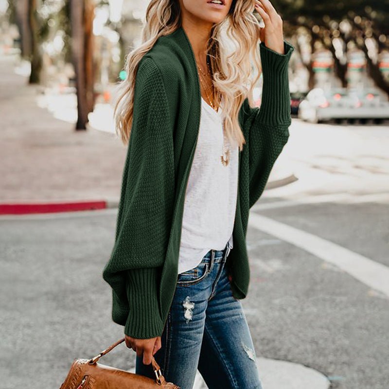 Frau in grüner Strickjacke, weißem T-Shirt und Jeans auf Straße, modische Herbstkleidung.