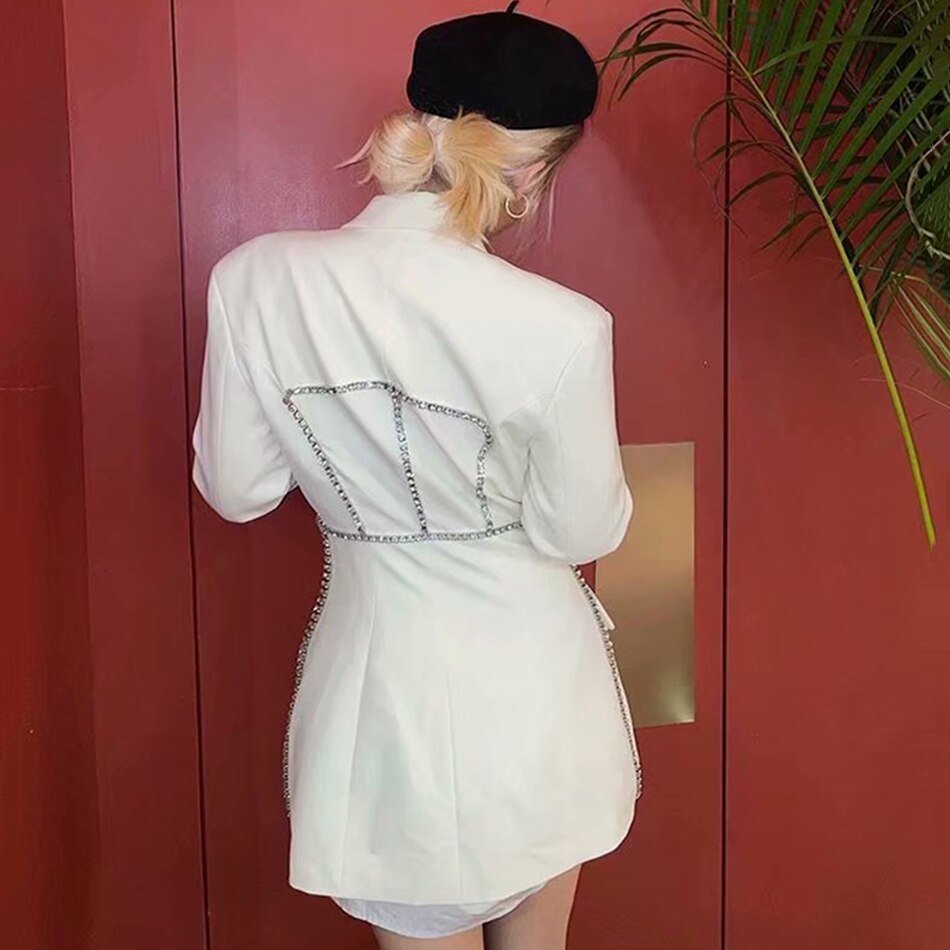 Frau in weißem Karo-Blazer mit langen Ärmeln und Ketten-Detail, modisch, elegant.