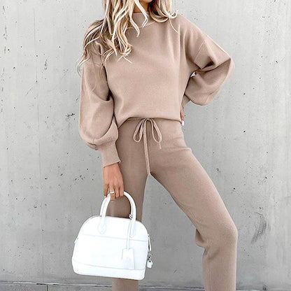 Frau in beigem Zweiteiler mit Rollkragen, High-Waist-Hose, weiße Handtasche, modisch, elegant.