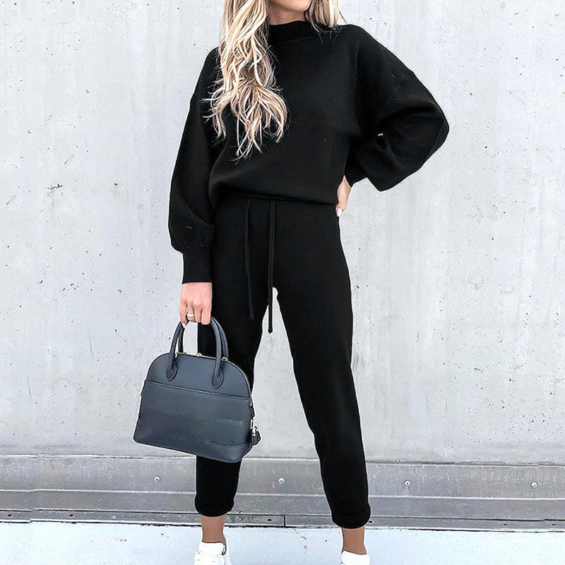 Frau in schwarzem Zweiteiler mit Rollkragen, High-Waist-Hose, hält schwarze Handtasche.
