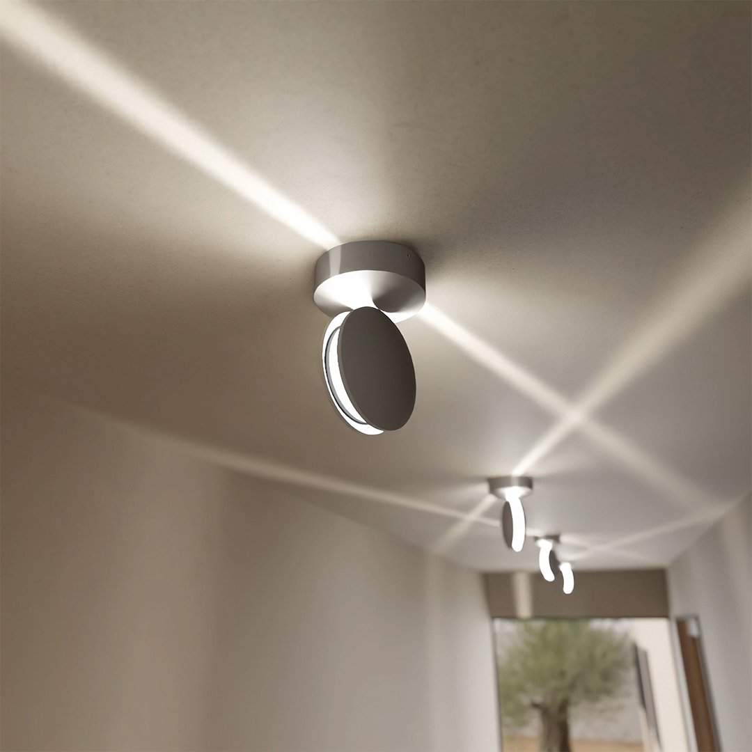 Lampa med vinklad rund skiva i taket sprider korsande ljusstrålar över taket i en korridor med flera lampor. 4