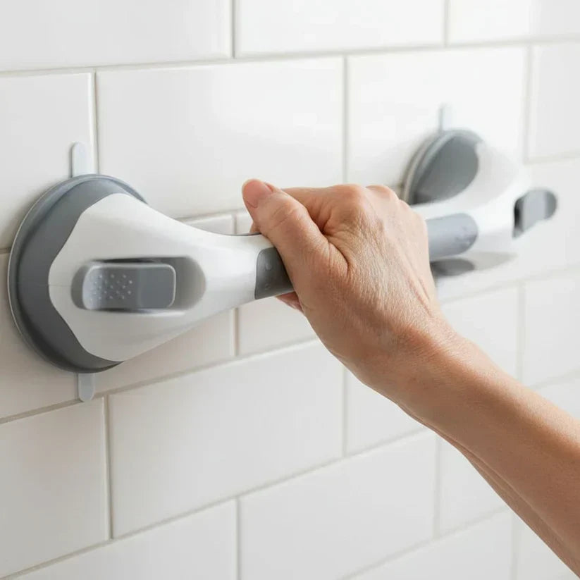 Närbild på en hand som greppar handtagets grå greppyta, med den ena sugkoppen och låsspaken synliga mot vita kakelplattor. 2