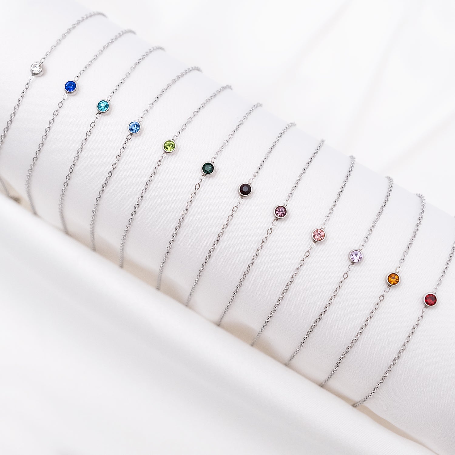Silberne Geburtsstein-Armbänder auf weißem Hintergrund, verschiedene Farben, Schmuck für Damen.